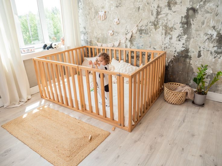 a baby in a crib next to a potted plant on the floor near a window