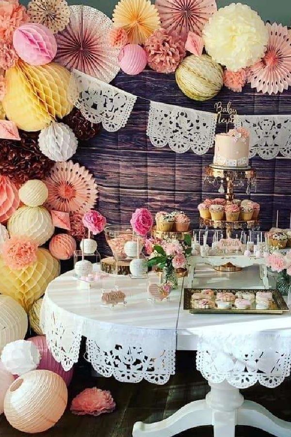 a table topped with cakes and cupcakes next to a wall covered in paper fans