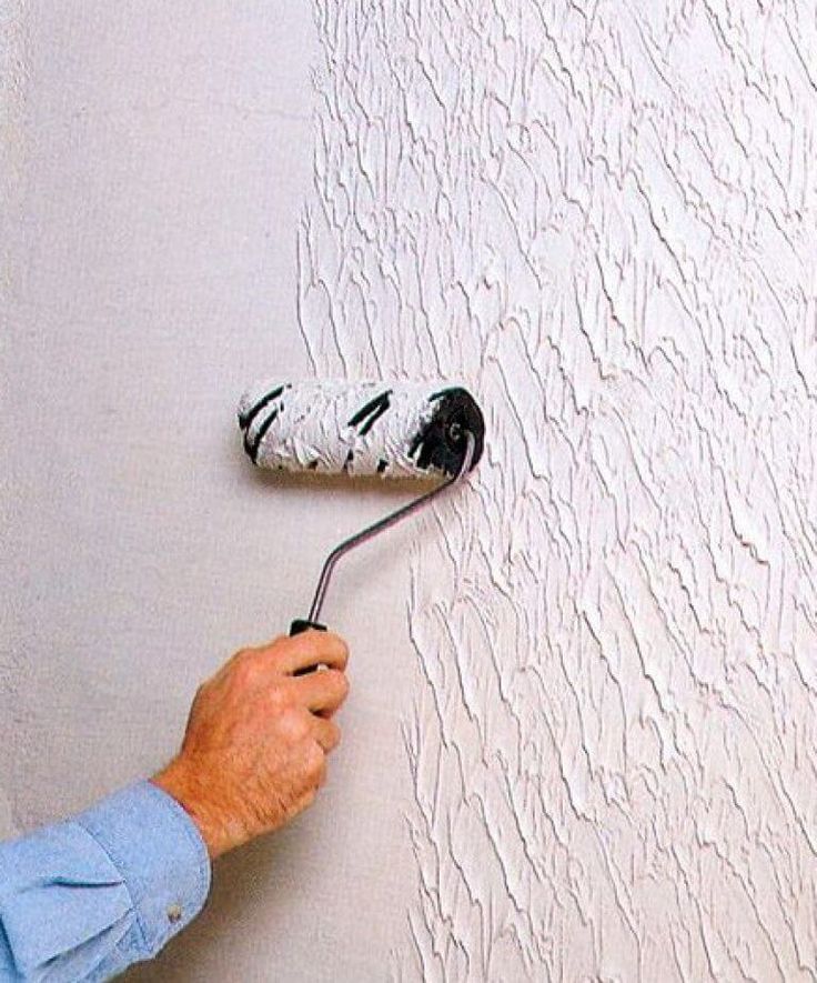 a man holding a paint roller in his hand and painting the wall with white paint