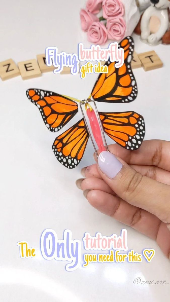 a hand holding a small butterfly on top of a white table next to flowers and scrabbles