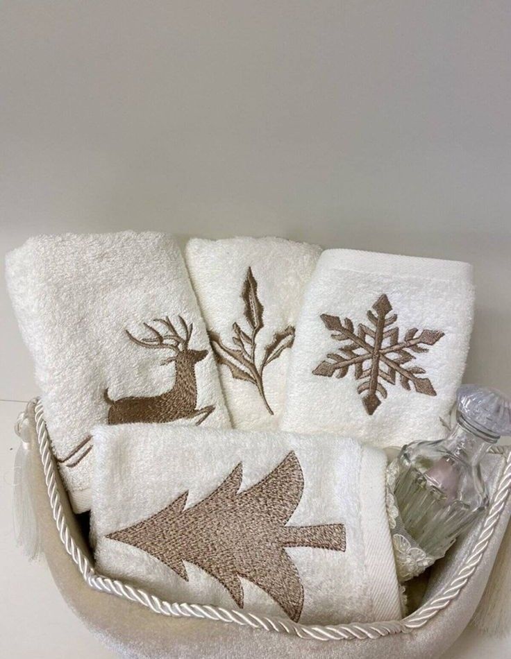 three white towels in a basket with deer and snowflake designs on the front