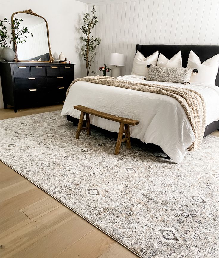 a bedroom with a bed, dresser and mirror on the wall next to hardwood flooring