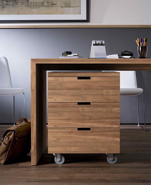 a wooden desk with drawers and a bag on the floor next to it in front of a chair