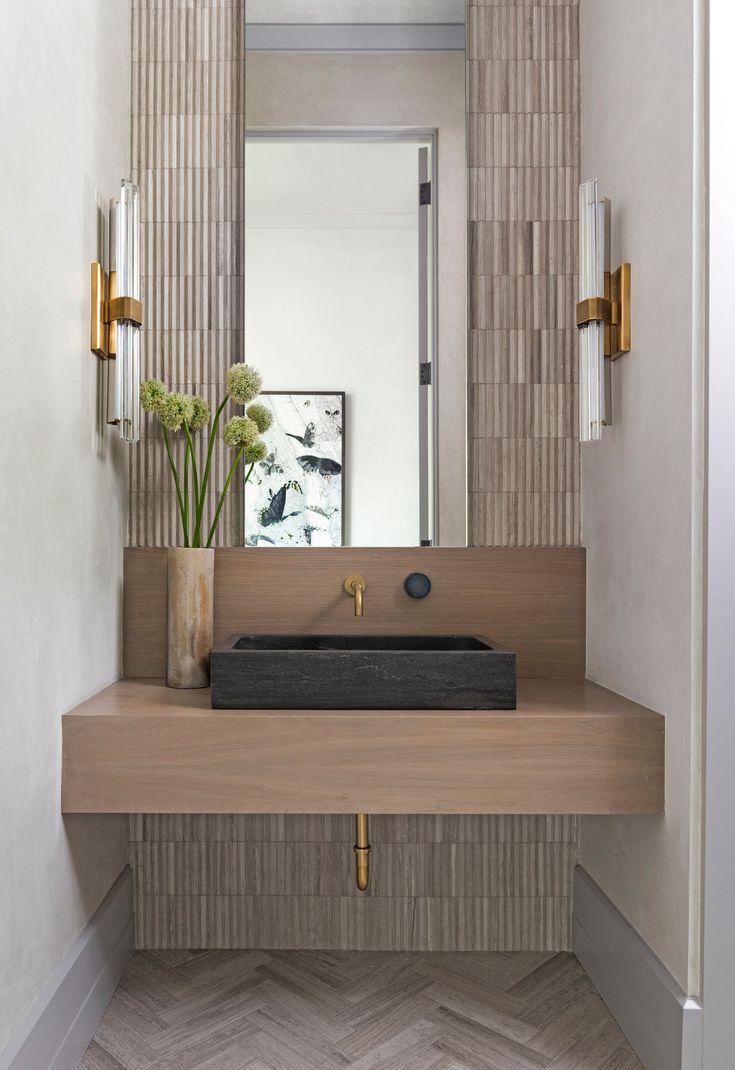 a bathroom sink sitting under a mirror next to a vase with flowers on top of it