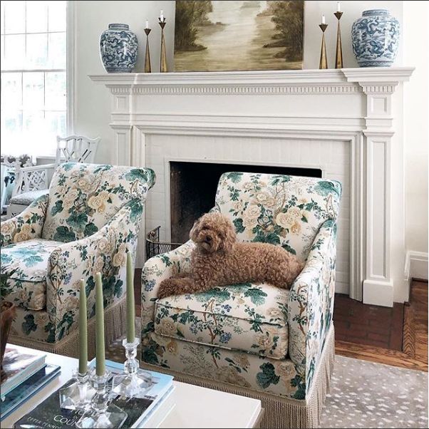 a dog sitting on a chair in front of a fire place with two vases