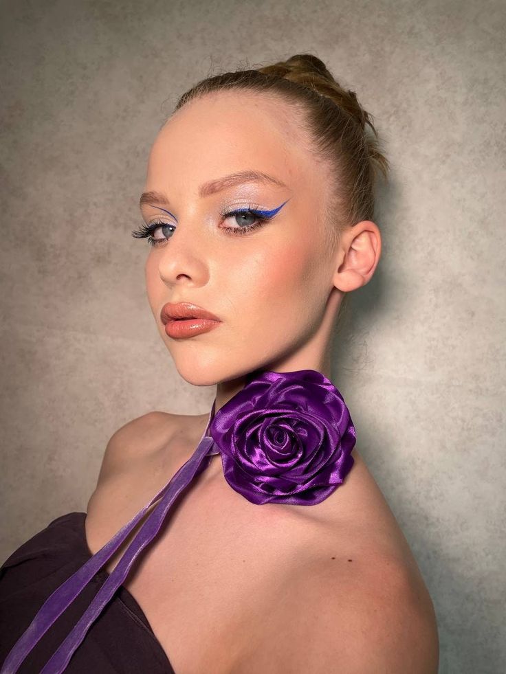 a woman wearing a purple flower on her neck with blue eyeshadow and makeup