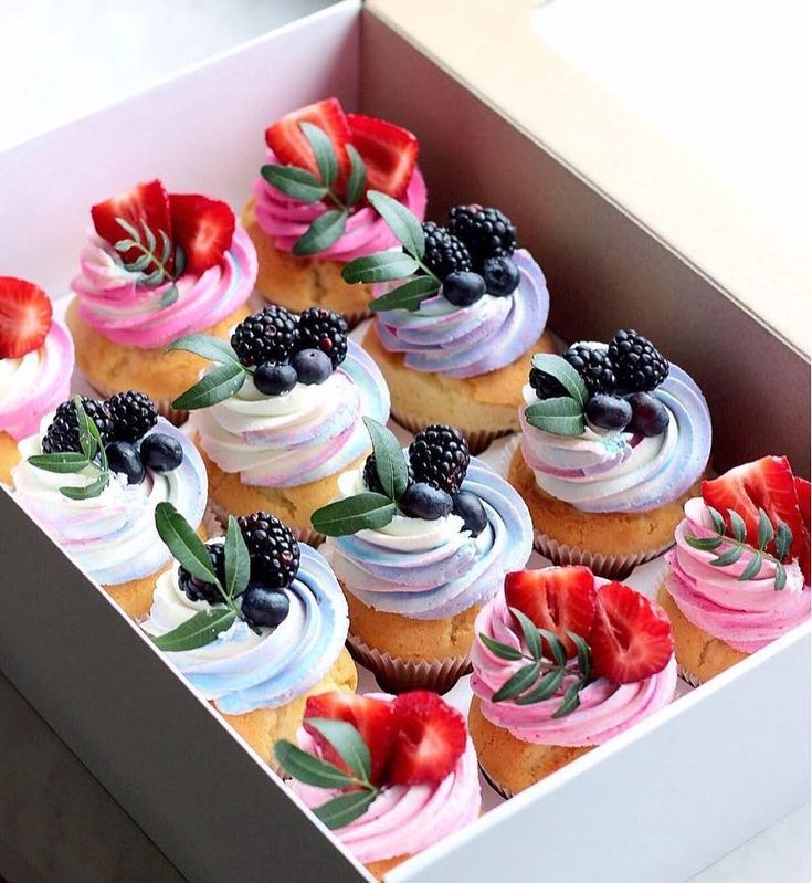 a box filled with cupcakes covered in frosting and berries