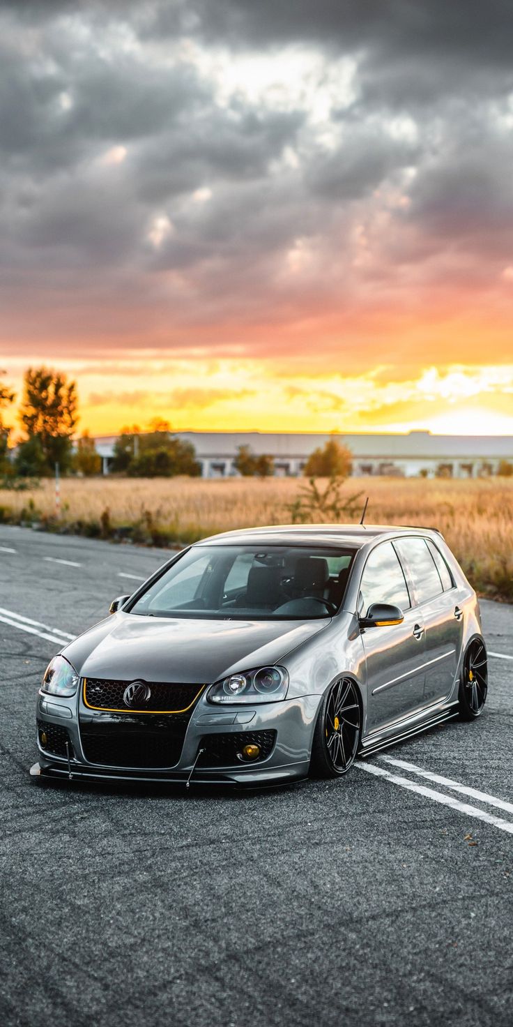 a silver car parked on the side of an empty road at sunset or dawn with clouds in the background