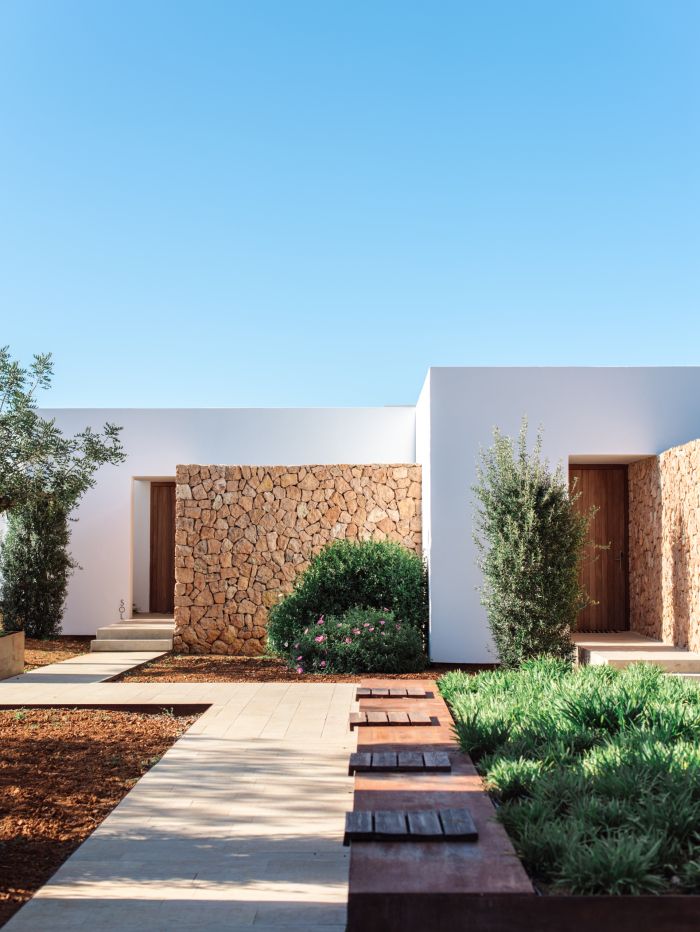 a modern house with stone walls and wooden steps leading up to the front door is surrounded by greenery