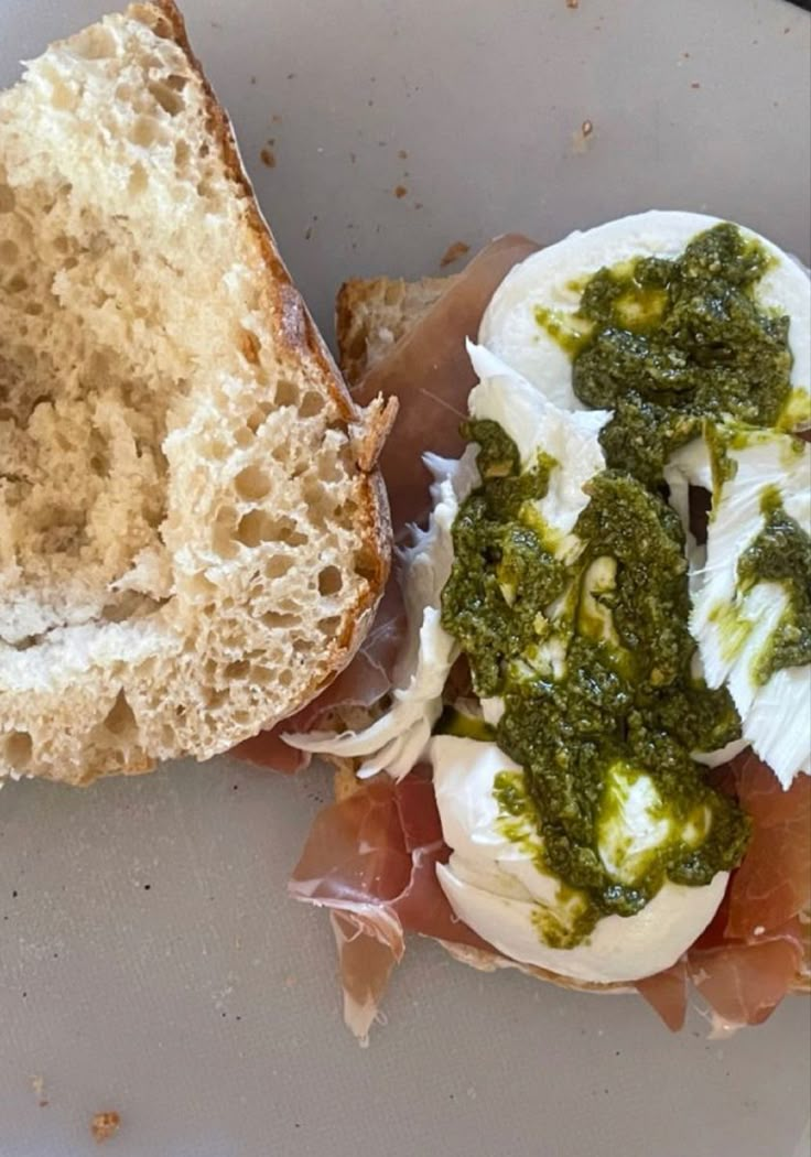 an open faced sandwich with pesto and cheese on it sitting on a white plate