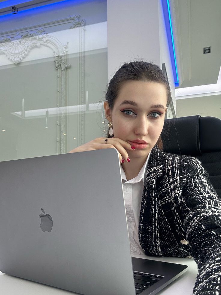 a woman sitting at a desk with a laptop in front of her, looking pensive