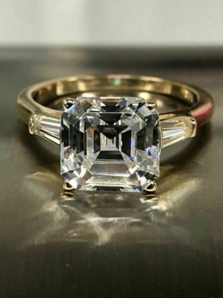 an emerald cut diamond ring with two baguets on the band and side stones