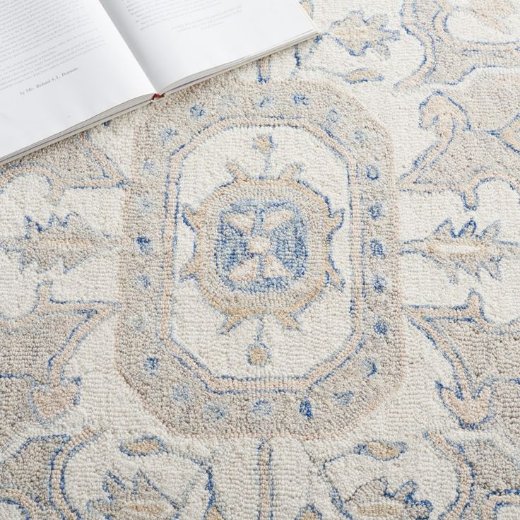 an open book sitting on top of a carpet covered in blue and white designs,