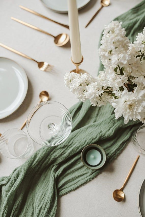 the table is set with white flowers and green napkins, silverware, and candles