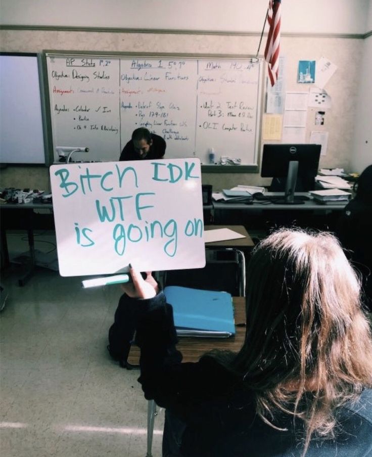 a person holding up a sign in front of a class room full of desks