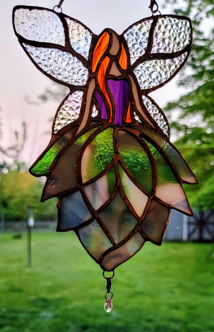 a stained glass sun catcher hanging from a chain in a yard with grass and trees