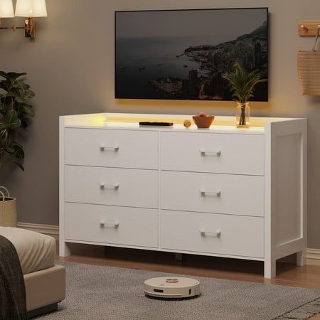 a white dresser in a living room with a television on the wall