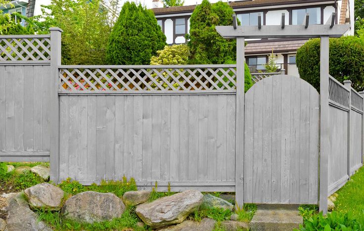 a wooden fence in front of a house with green grass and rocks on the ground