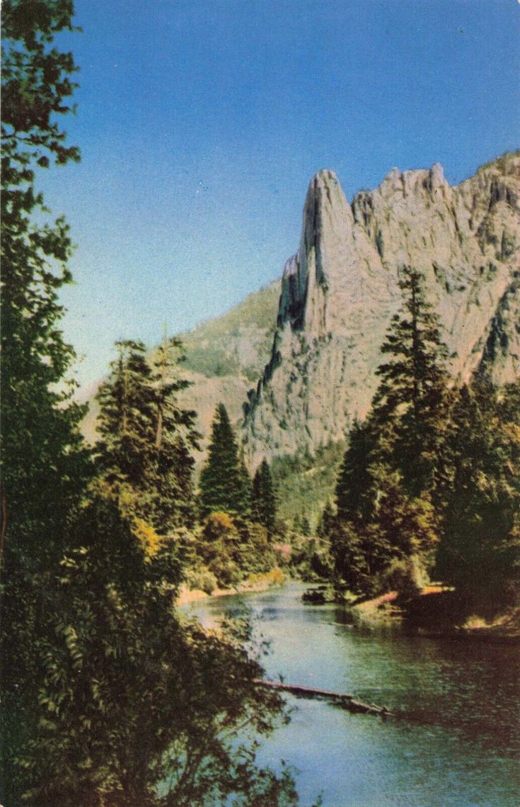 an old photo of a mountain with trees around it and a river in the foreground