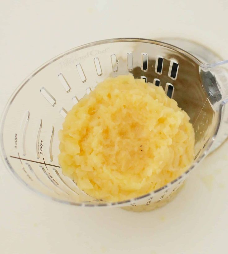 mashed potatoes in a blender with a metal strainer next to it on a white surface