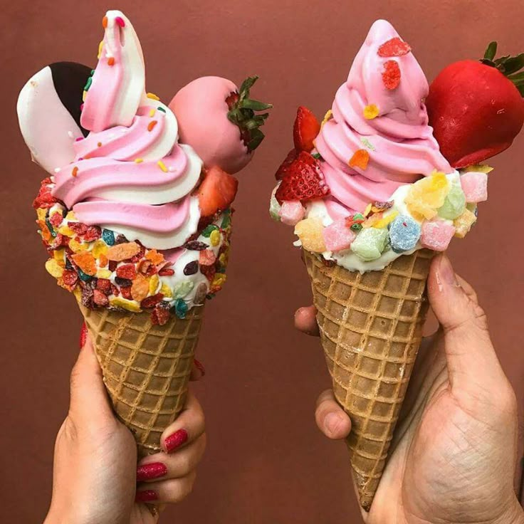 two people holding ice cream cones with fruit toppings on them, one is pink and the other is white