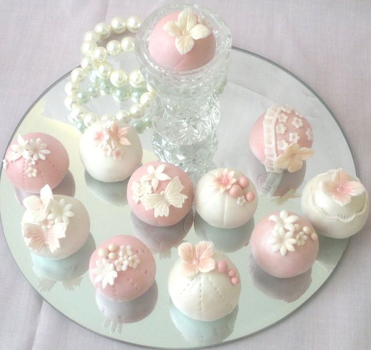 there are many small cakes on the glass platter with pearls and beads around them