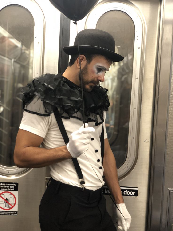 a man with white face paint and black hair is standing in front of a train door