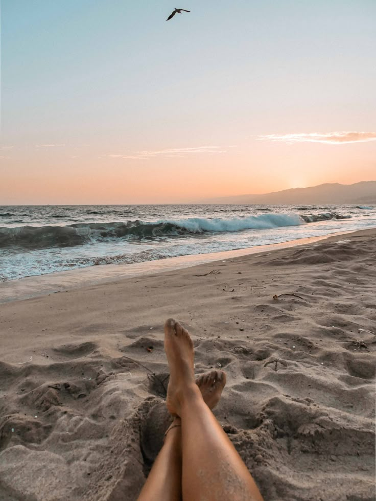 a person laying on top of a beach next to the ocean with their feet in the sand