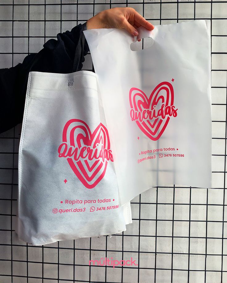 two shopping bags with logos on them are held by someone's hand in front of a tiled wall