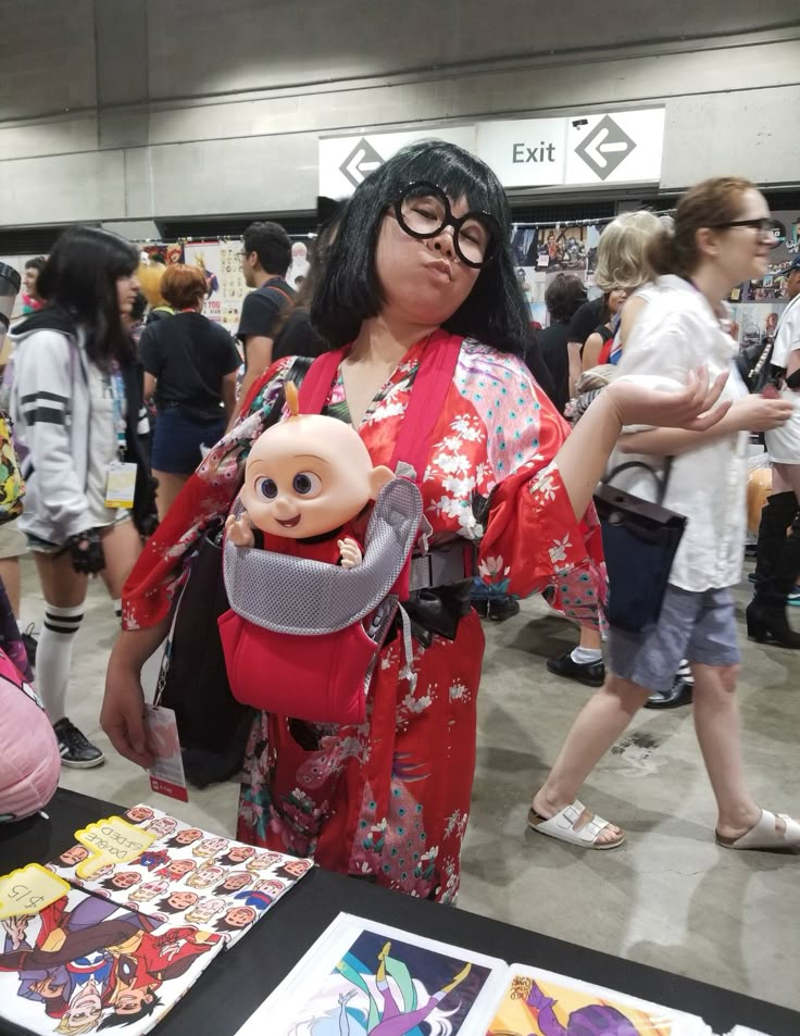 a woman in a kimono holding a doll at an event with other people around her