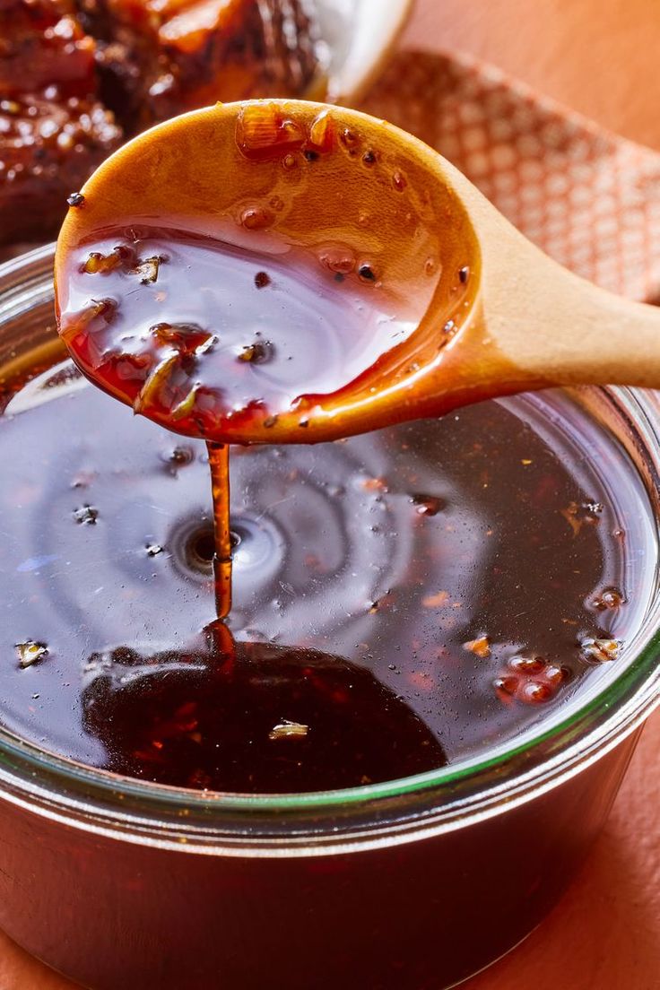 a spoon full of honey sitting on top of a jar filled with liquid and sauce