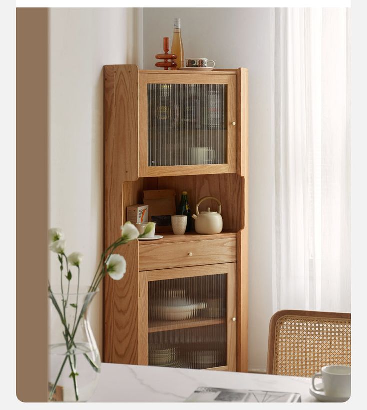 a wooden cabinet with glass doors and drawers in the corner next to a vase filled with flowers