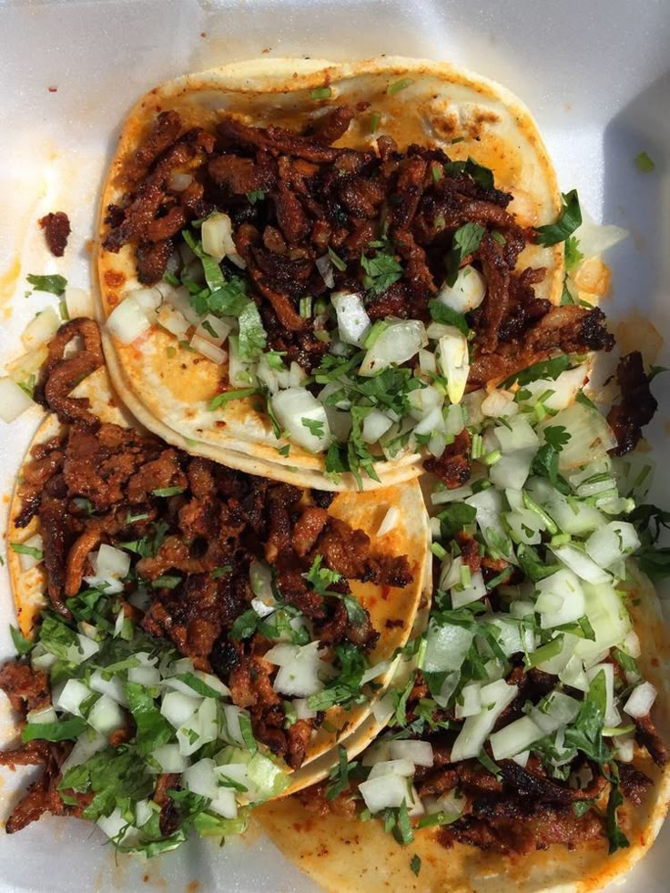 three tacos filled with meat, onions and cilantro on top of a white tray