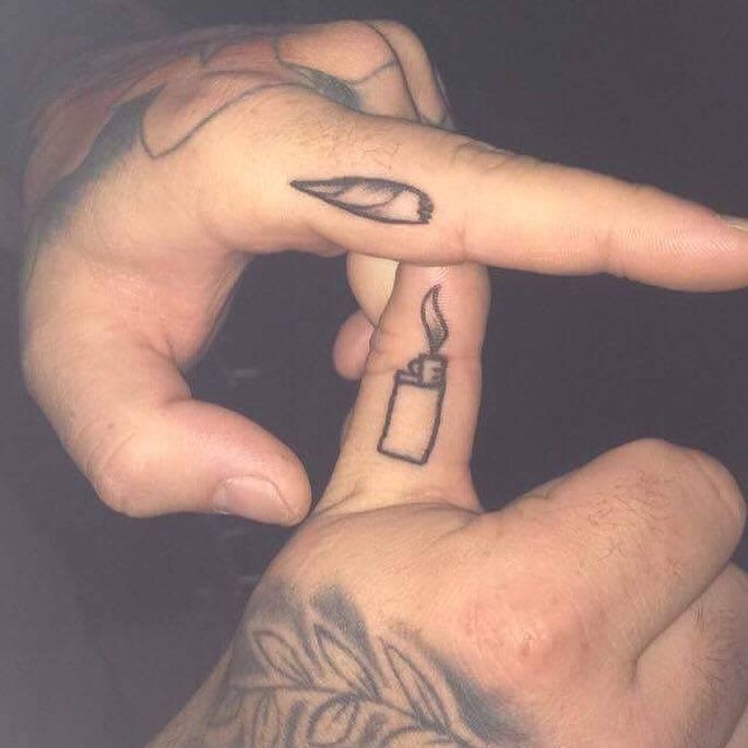 two fingers with tattoos on them are pointing to the side and one has a lighter tattoo on it