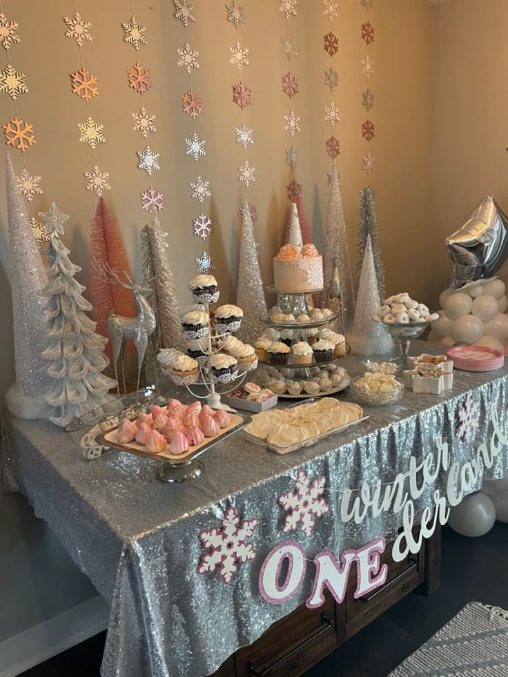 a table topped with lots of desserts and cupcakes next to a wall covered in snowflakes