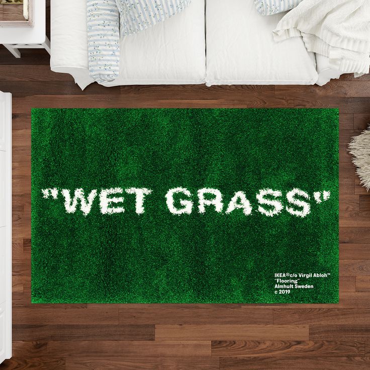 a green rug with the words wet grass written on it in white letters next to a bed