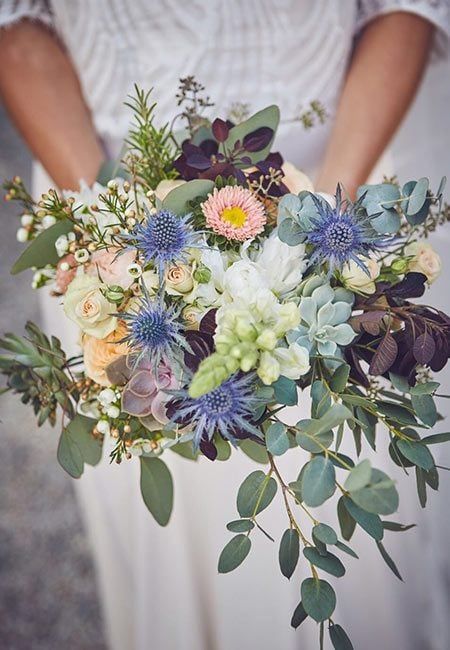 a bride holding a bouquet of flowers and greenery