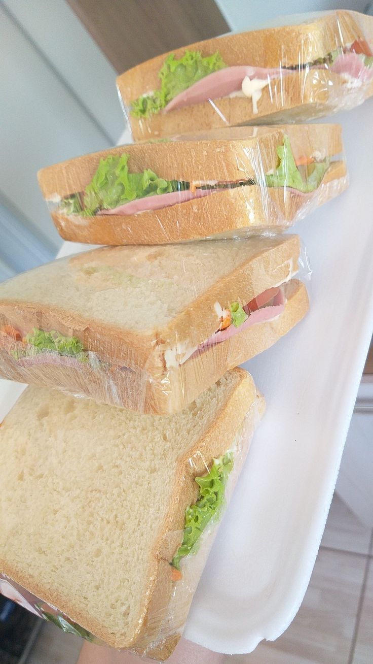 three sandwiches are stacked on top of each other in plastic wrappers and being held by someone's hand