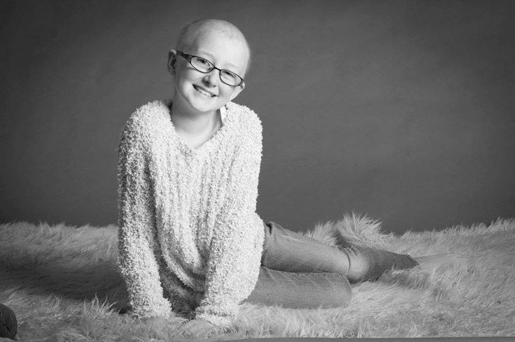 a black and white photo of a smiling woman wearing glasses sitting on a furry rug