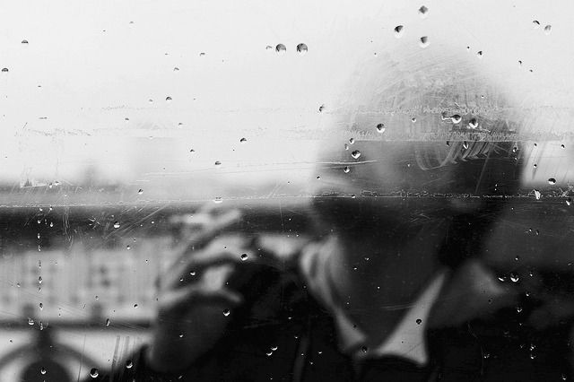 a man taking a photo through a rain soaked window