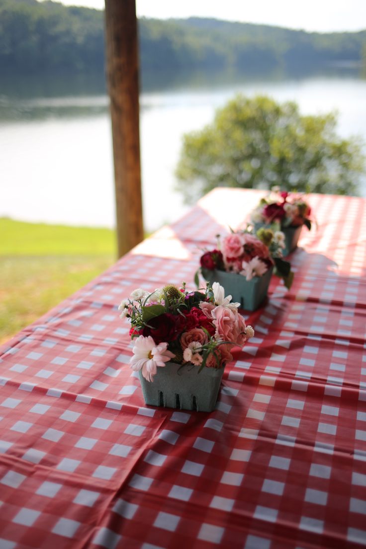 flowers are lined up on the table at an outdoor gathering by the water's edge