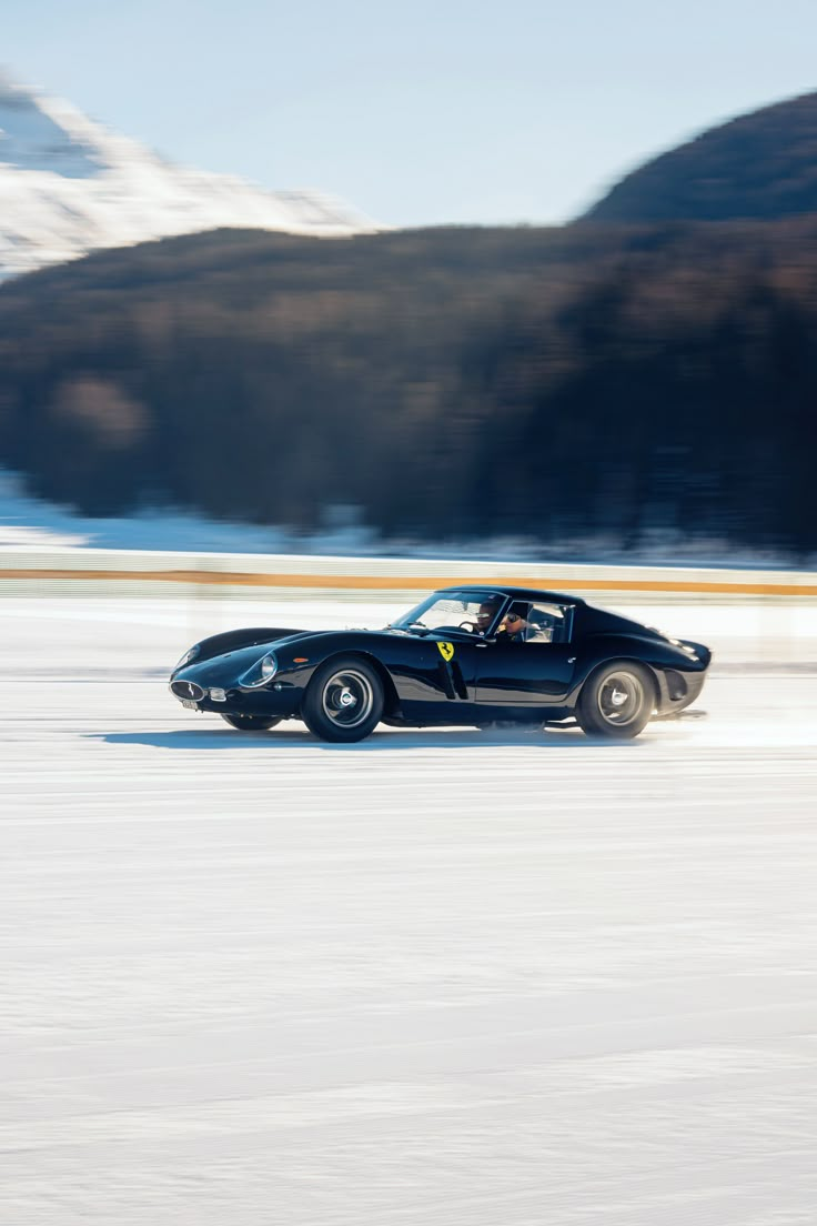 a black sports car driving on snow covered ground with mountains in the backgroud