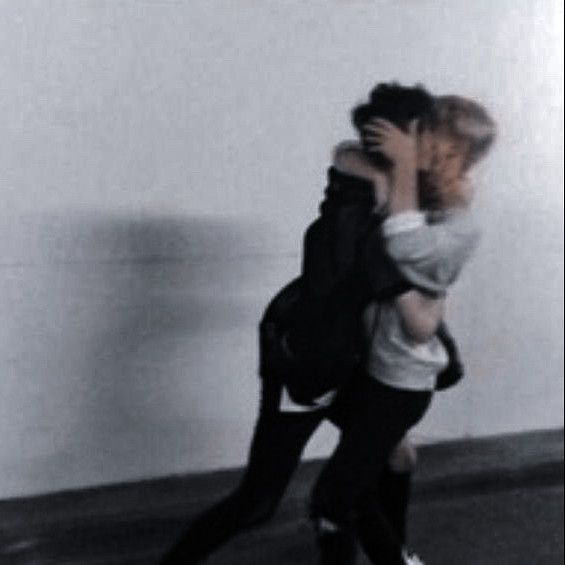 two people are hugging in the middle of an empty room with white walls and black flooring