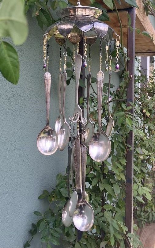 a chandelier with spoons hanging from it's sides and green plants in the background