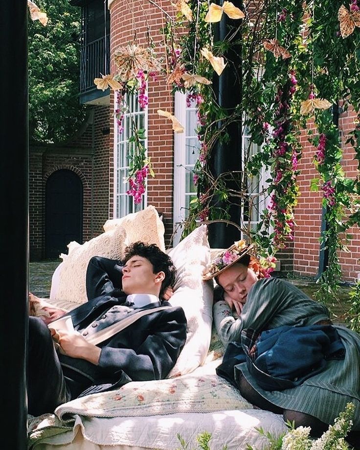 two young men laying on top of a white couch in front of a brick building