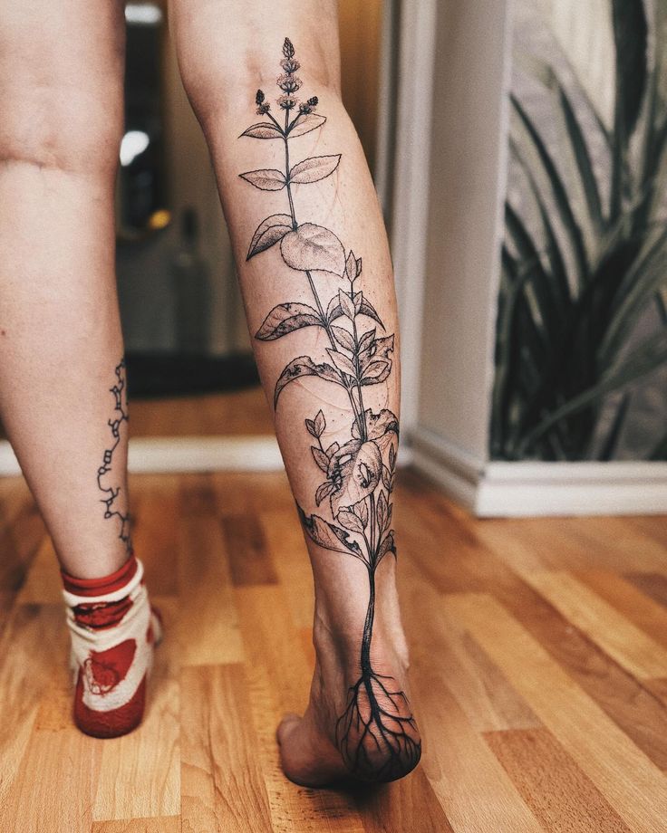 a woman's legs with tattoos on them and flowers in the bottom part of her leg