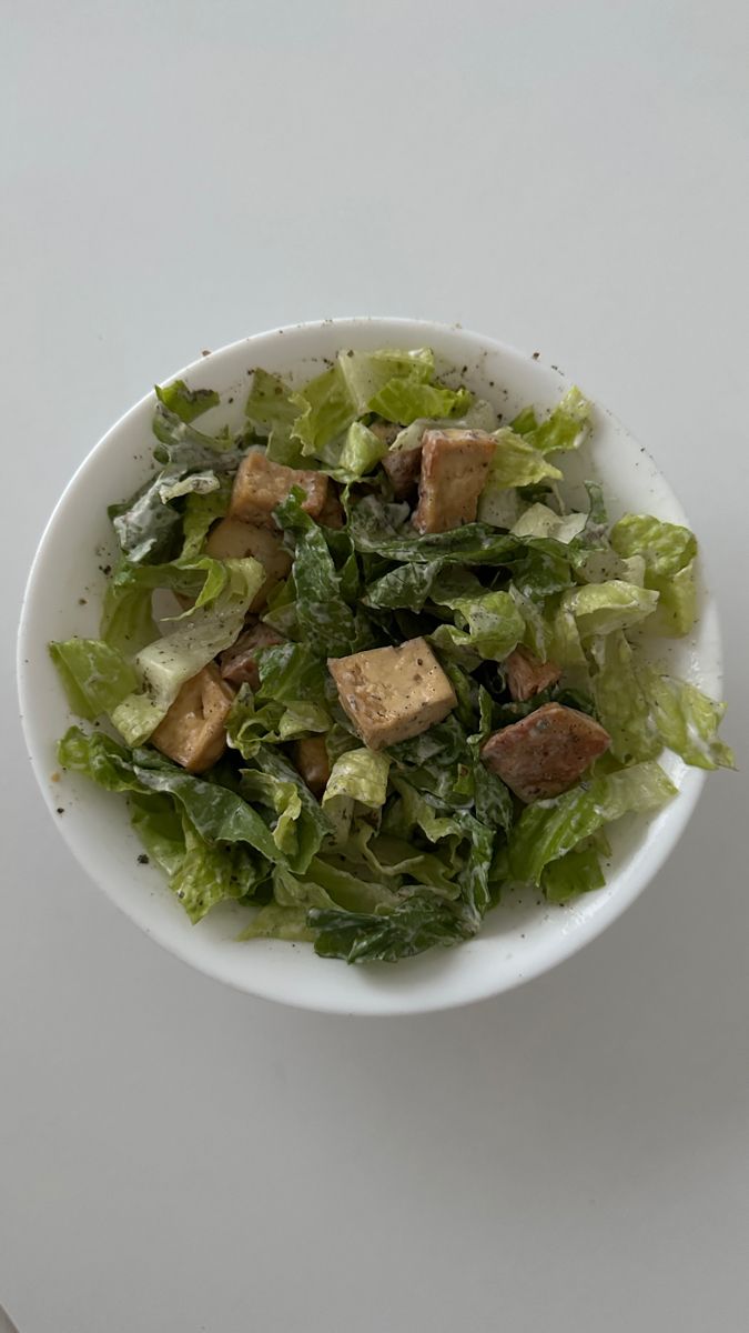 a white bowl filled with lettuce and tofu on top of a table