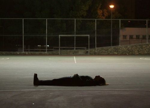 a person laying on the ground in an empty parking lot at night with a street light behind them