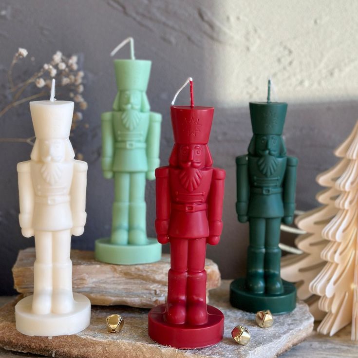 small candles in the shape of toy soldiers sit on a piece of wood next to christmas trees