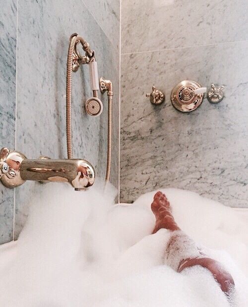 a person laying in a bathtub filled with foam and water next to a shower head